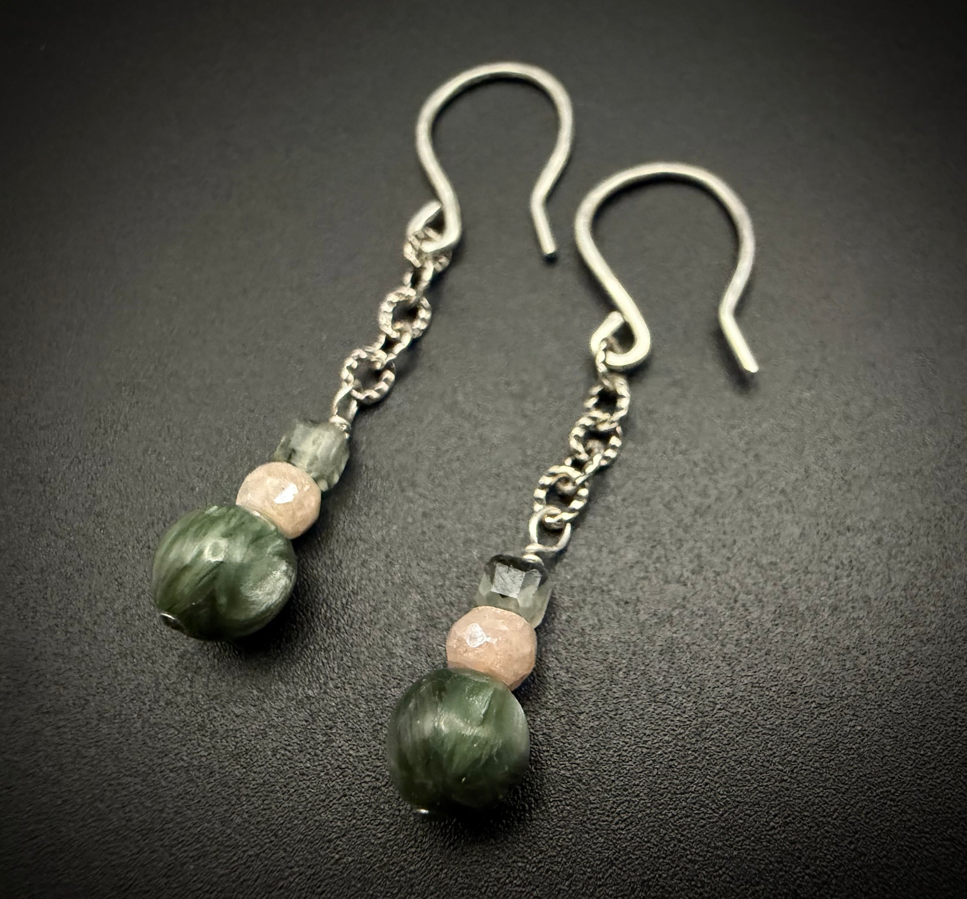 Handcrafted Lily Drops earrings featuring stacked beads of green Prehnite, peach moonstone, and dark green Seraphinite on sterling silver wires.