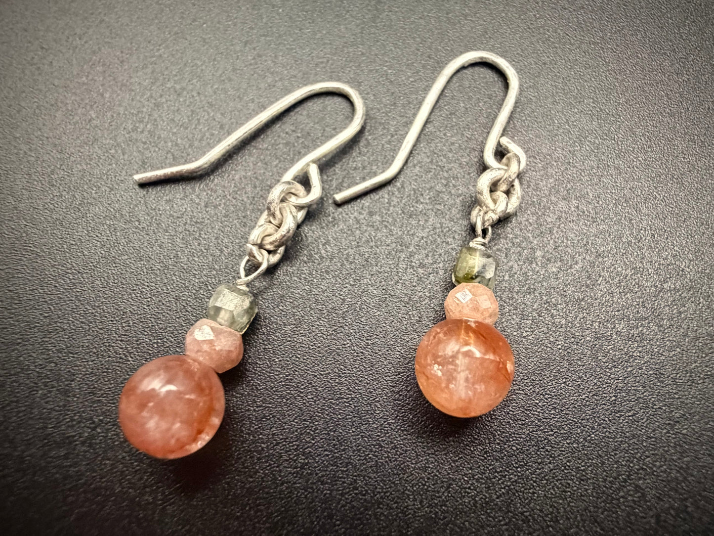 Close-up of Dahlia Drops earrings on a dark surface, featuring stacked Red Agate, Peach Moonstone, and Prehnite beads with sterling silver hooks.