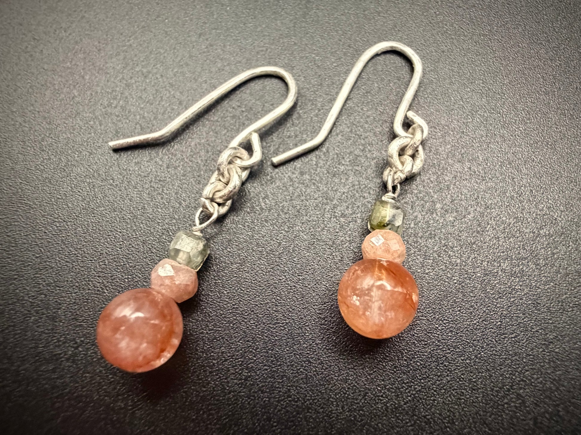 Close-up of Dahlia Drops earrings on a dark surface, featuring stacked Red Agate, Peach Moonstone, and Prehnite beads with sterling silver hooks.