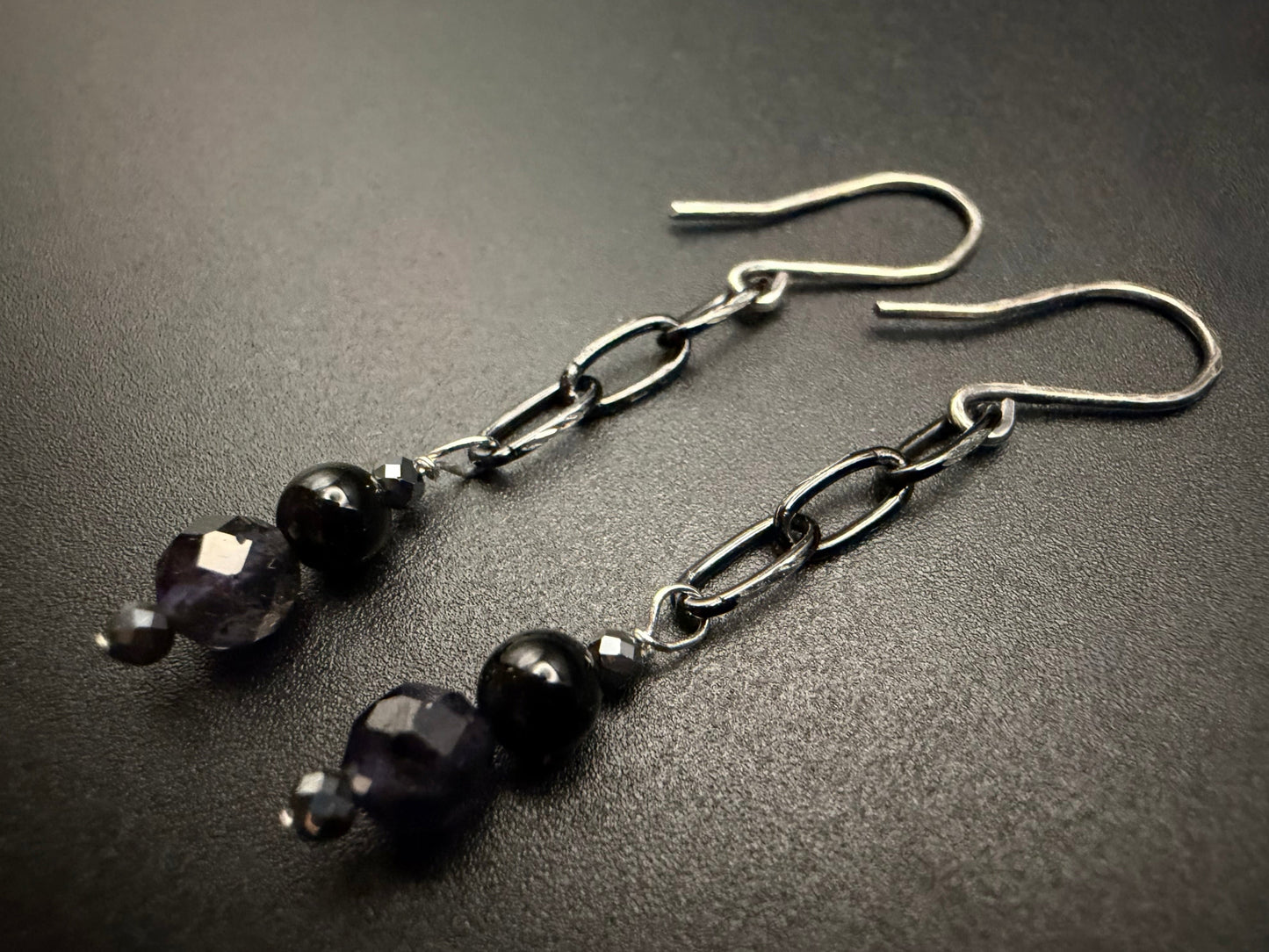 Handcrafted sterling silver drop earrings featuring a tiered arrangement of faceted iolite, smooth onyx, and metallic hematite beads suspended from a delicate silver chain.