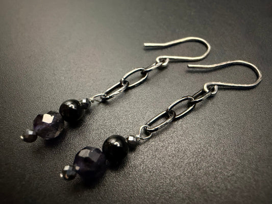 Handcrafted sterling silver drop earrings featuring a tiered arrangement of faceted iolite, smooth onyx, and metallic hematite beads suspended from a delicate silver chain.
