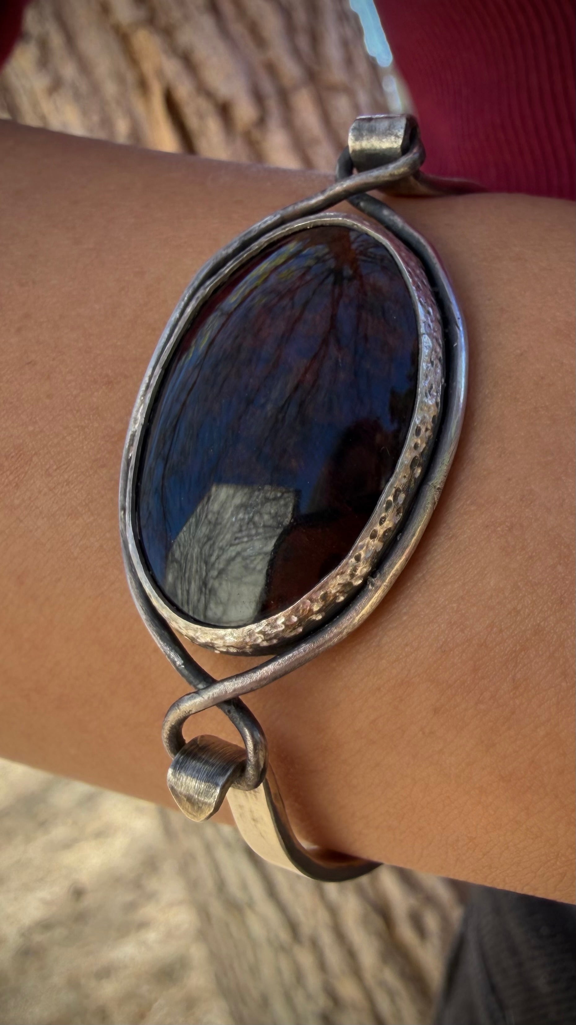 A person wearing the Rootvaern Cuff, a handcrafted sterling silver bracelet with a large mahogany obsidian stone, showcasing its petite XS fit and rugged, weathered texture.