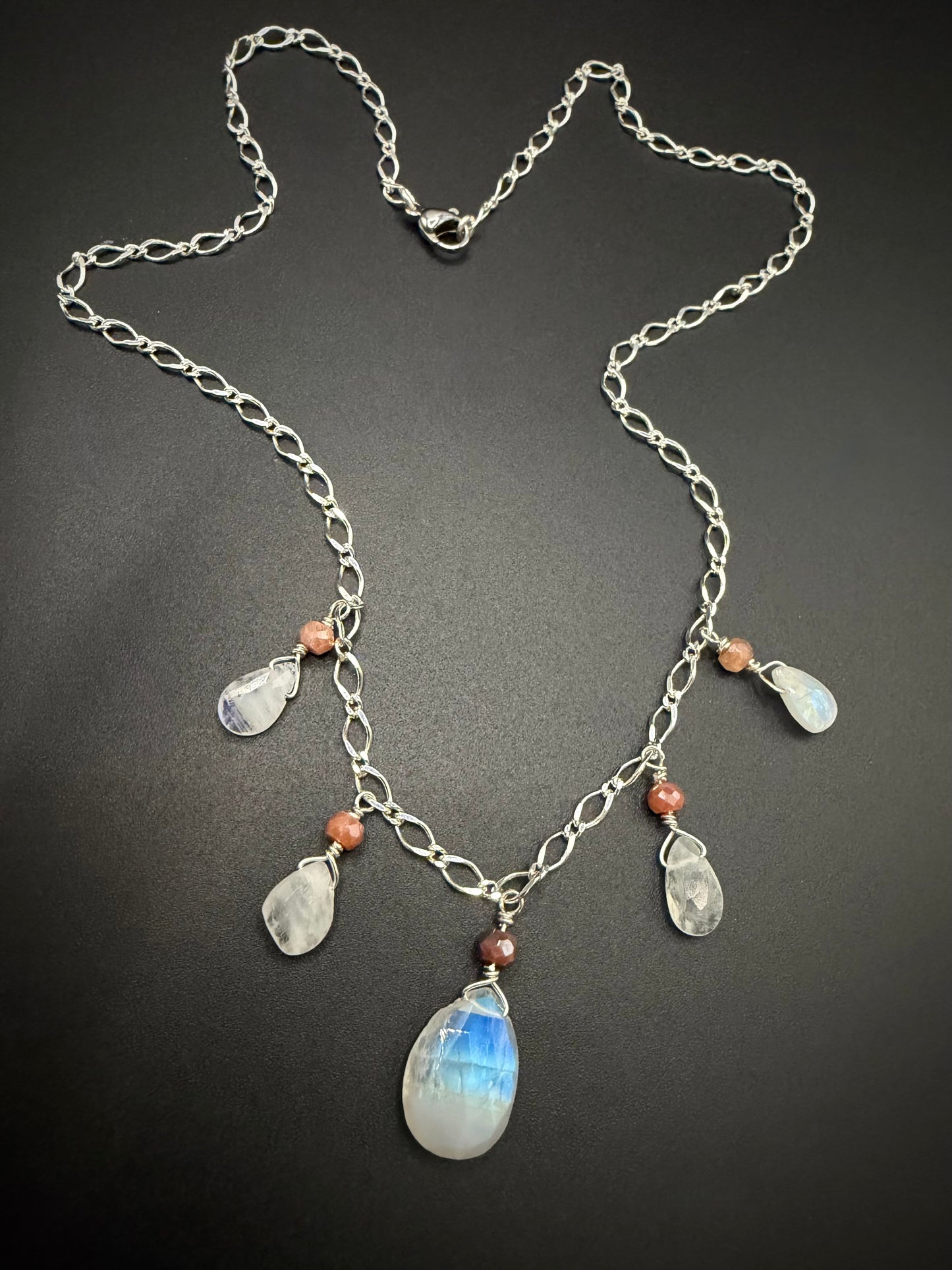 Handcrafted sterling silver necklace featuring teardrop-shaped rainbow moonstone and small round peach moonstone beads suspended from a delicate silver chain.