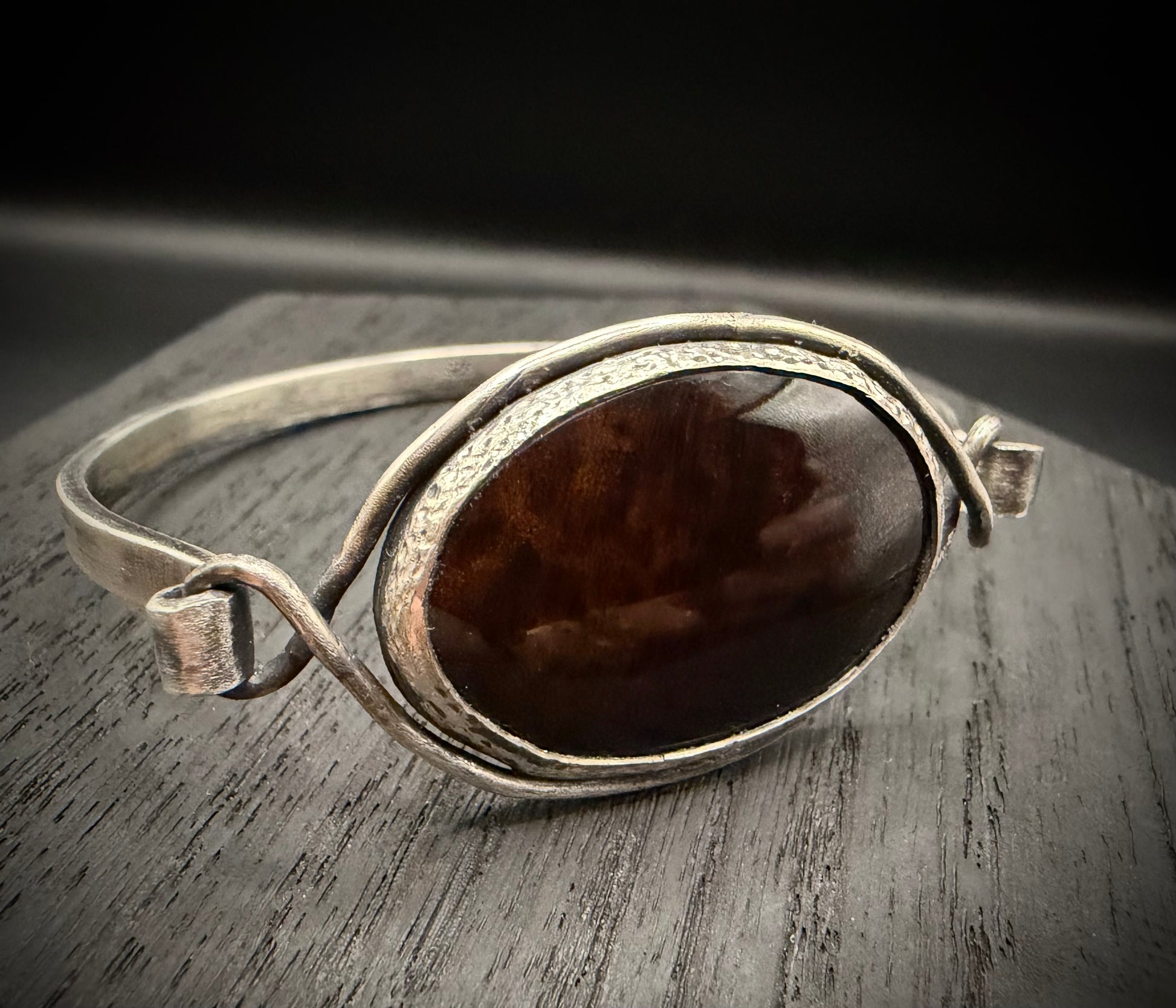 Handcrafted sterling silver cuff bracelet featuring a large, oval mahogany obsidian stone with natural reddish-brown volcanic patterns and a hand textured, weathered texture.