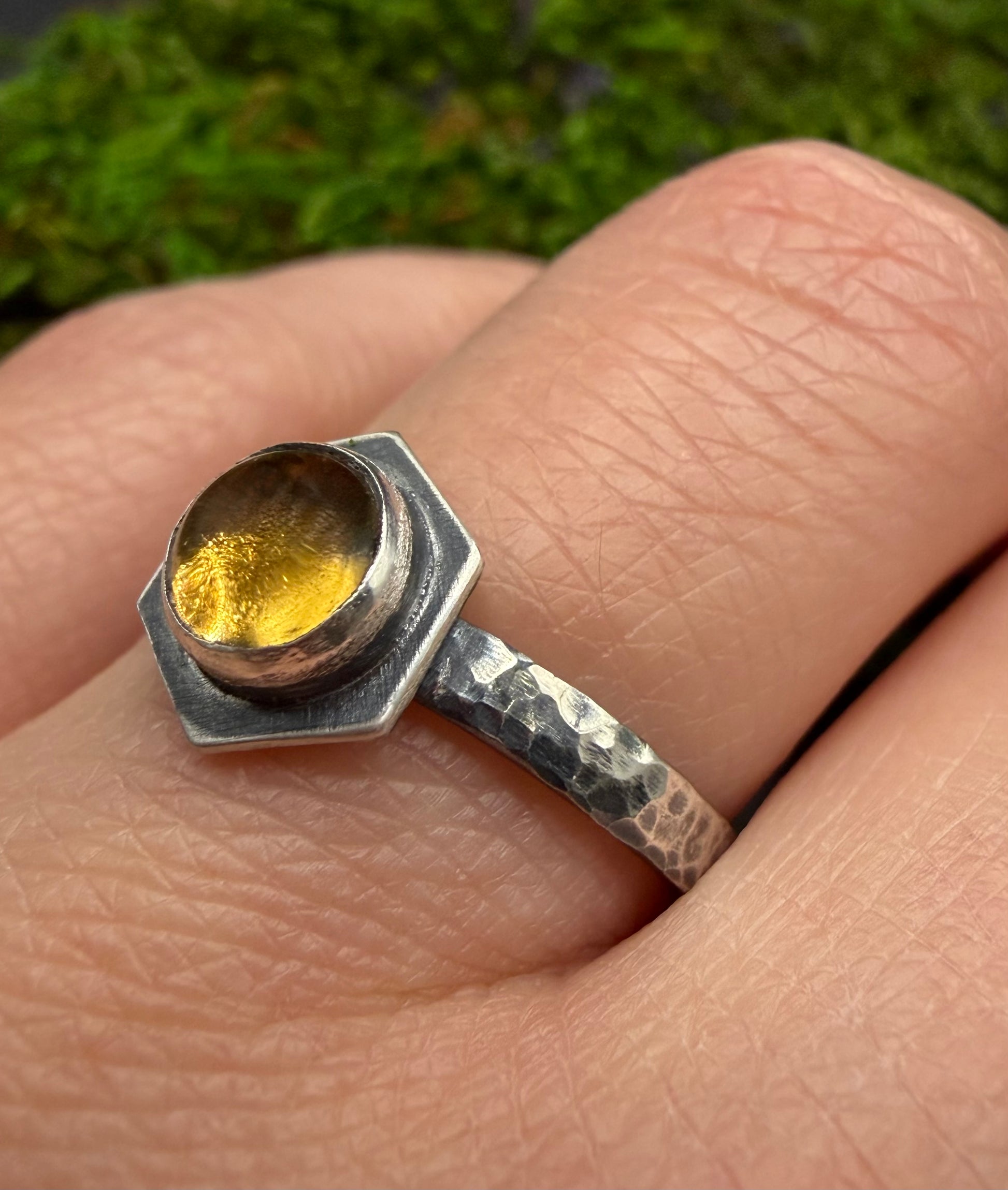 Close-up of the Solaire Ring on a finger, featuring a vibrant hexagonal citrine stone set in a heavy, hand-hammered sterling silver band with an oxidized, moody finish.