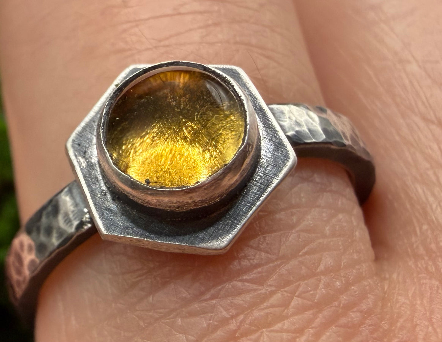 Close-up of the Solaire Ring on a finger, featuring a textured hexagonal center set in a heavy, hand-hammered sterling silver band.