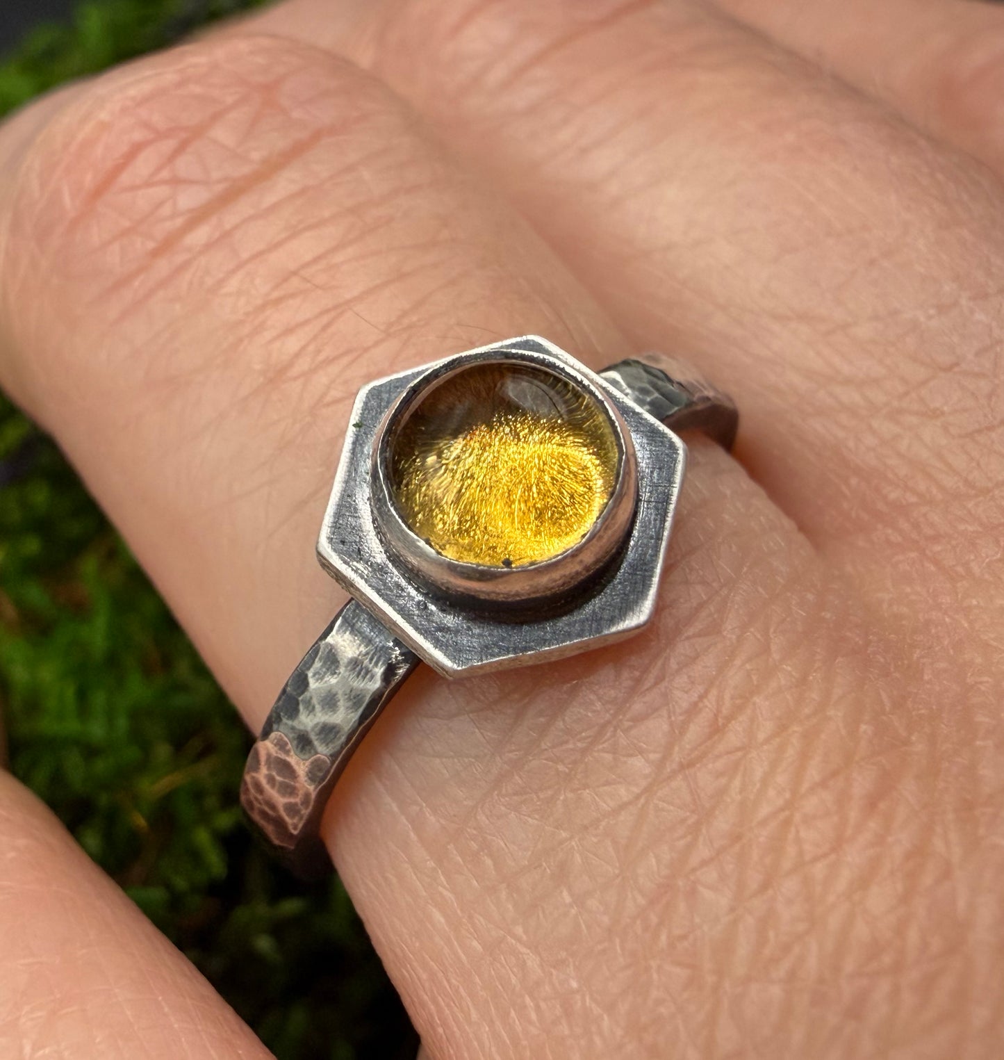 Close-up of the Solaire Ring worn on a finger, featuring a hexagonal center stone with gold leaf detail set in a heavy, hand-hammered, textured sterling silver band.