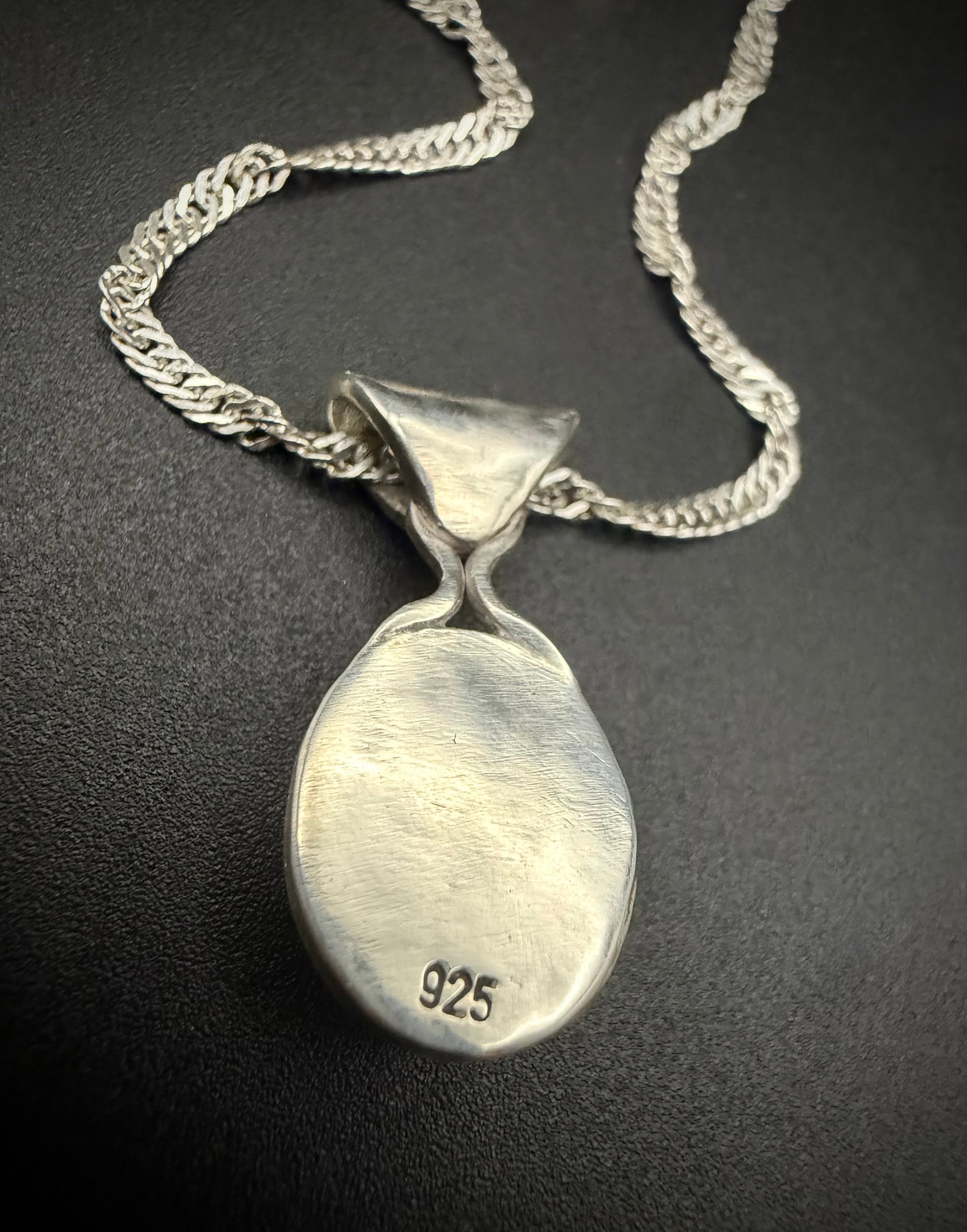 The reverse side of the handcrafted sterling silver Lavinia pendant against a dark, matte background. The image highlights the "925" hallmark stamped cleanly near the bottom of the smooth silver backplate. The silver chain is elegantly draped above the flared bale, showcasing the solid construction of the piece.