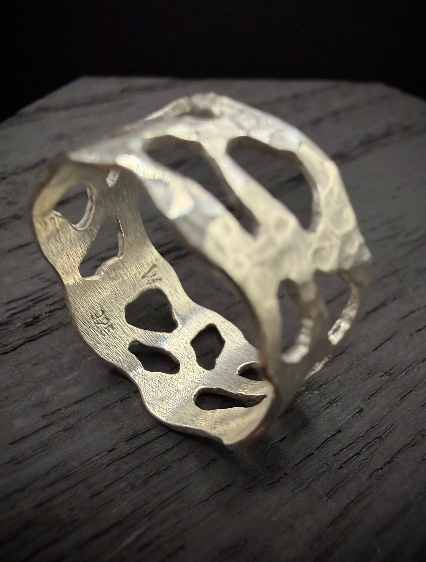 Close-up studio shot of the handcrafted sterling silver wide band ring. The image emphasizes the deep, heavily hammered texture and the crisp, dark oxidized edges of the organic geometric cutouts.