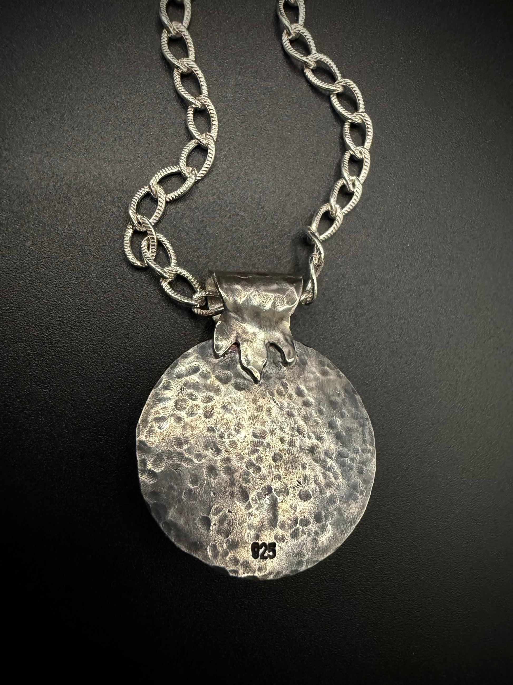 The reverse side of a handcrafted sterling silver pendant, showcasing a clean, heavily hammered metal texture, a secure fine silver bezel setting, a 925 silver hallmark stamp near the bottom, and a stylized textured leaf bail on a silver chain.