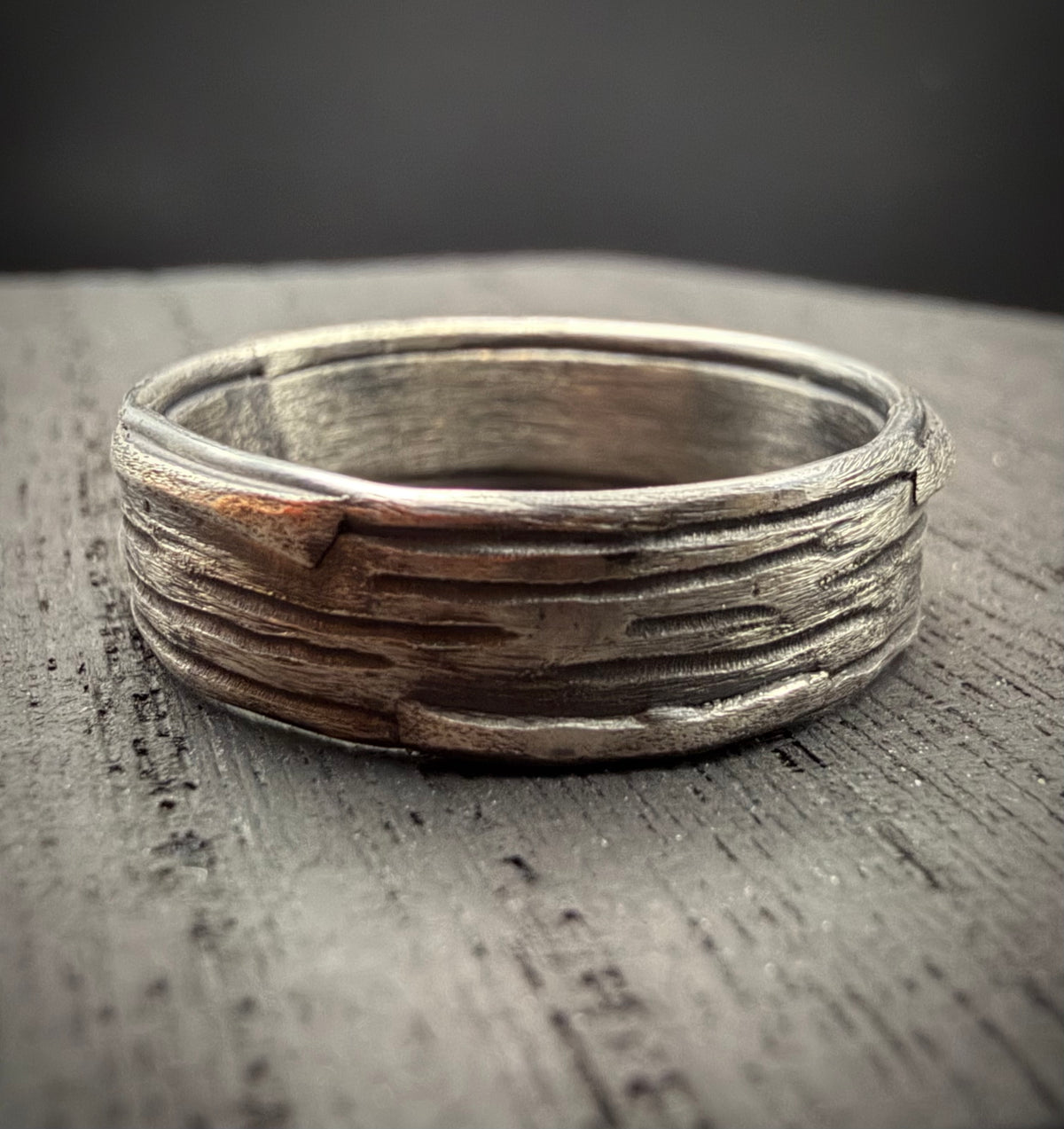Handcrafted sterling silver Rune Ring featuring a rustic, bark-like texture resting on a weathered wood surface.