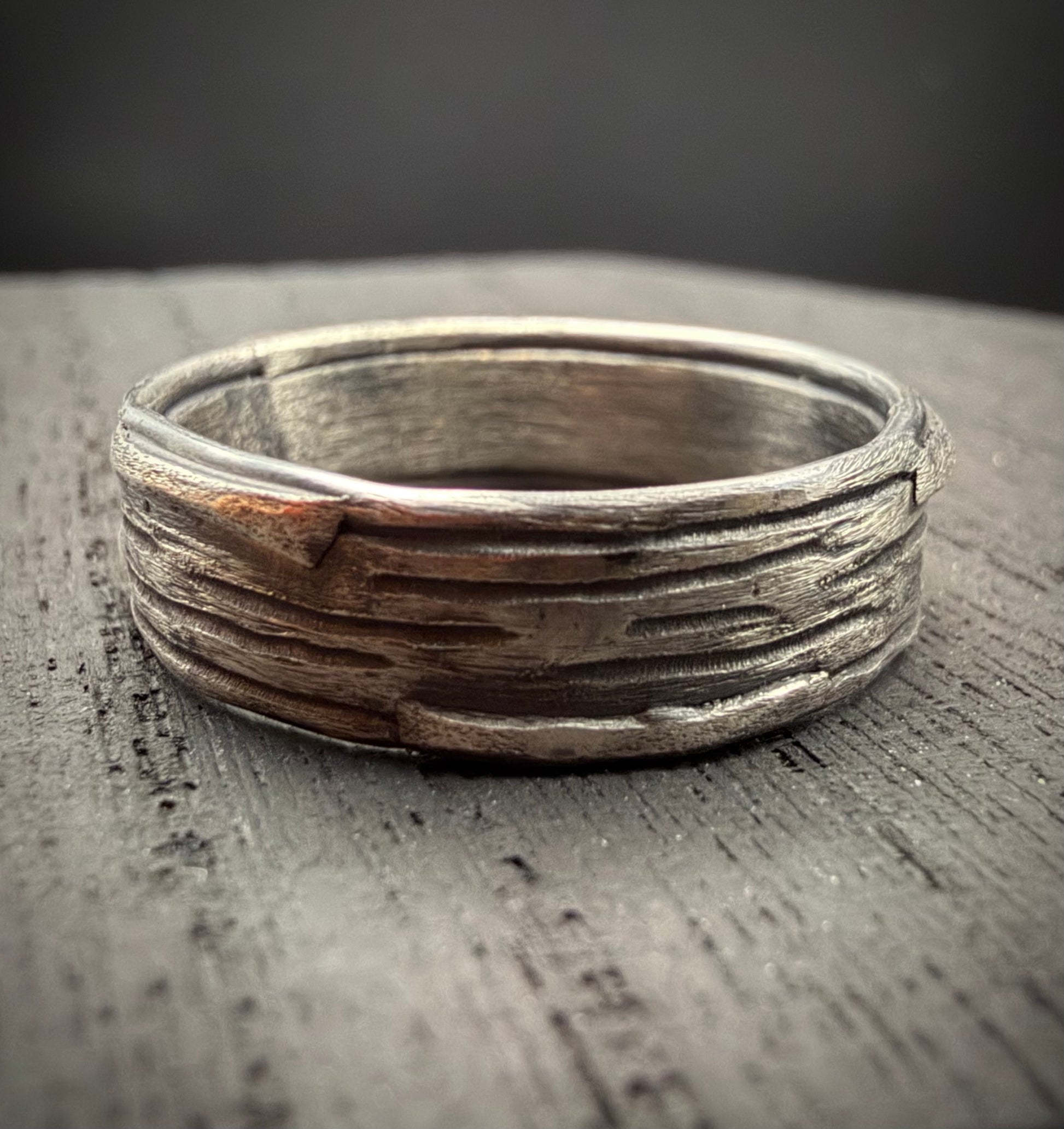 Handcrafted sterling silver Rune Ring featuring a rustic, bark-like texture resting on a weathered wood surface.