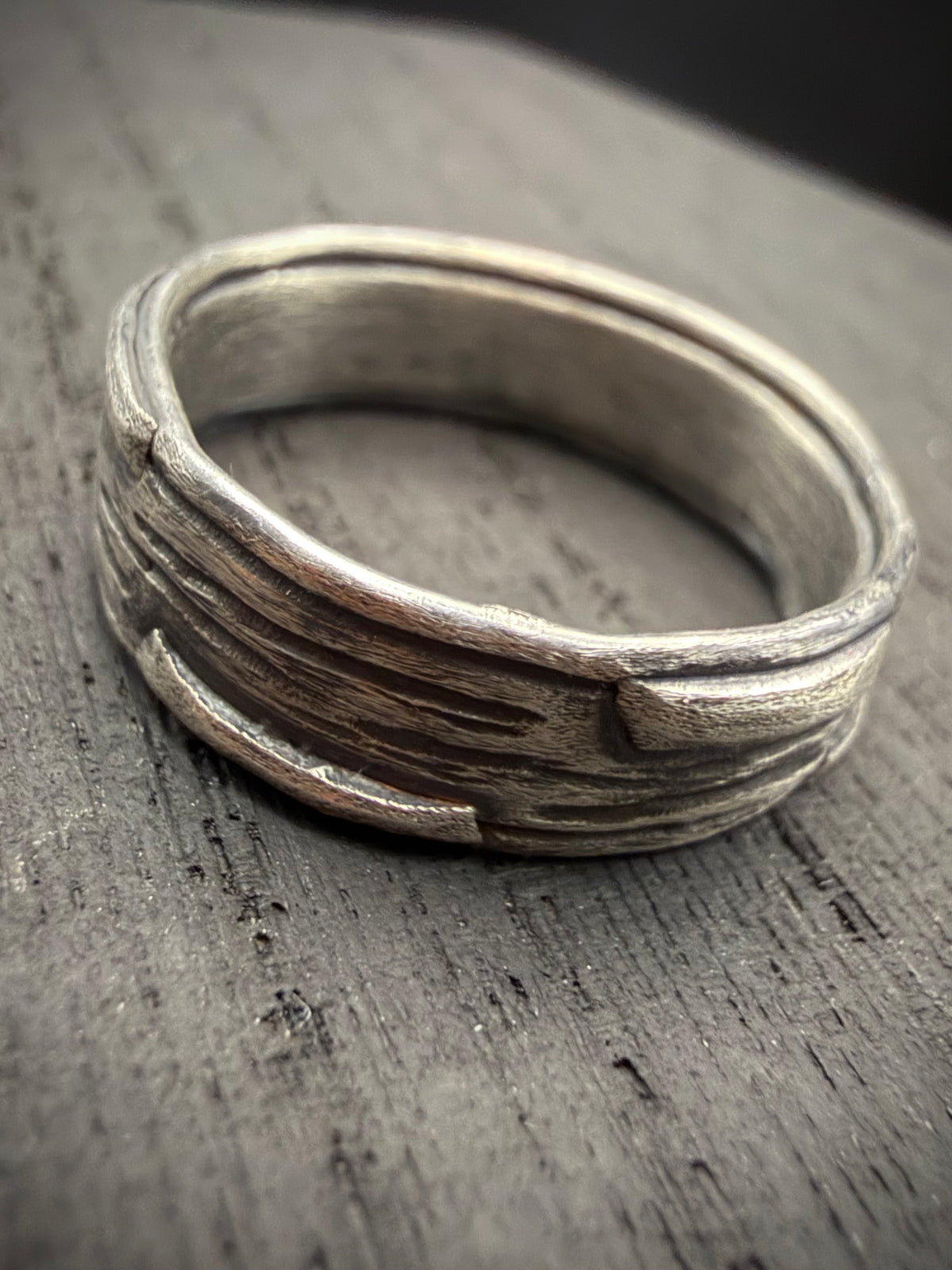 Handcrafted sterling silver Rune Ring with a textured wood-grain pattern resting on a rustic wooden surface.