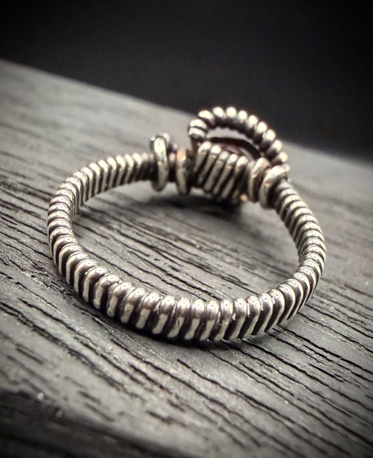 Handcrafted wire-wrapped sterling silver ring resting on a dark weathered wood surface.