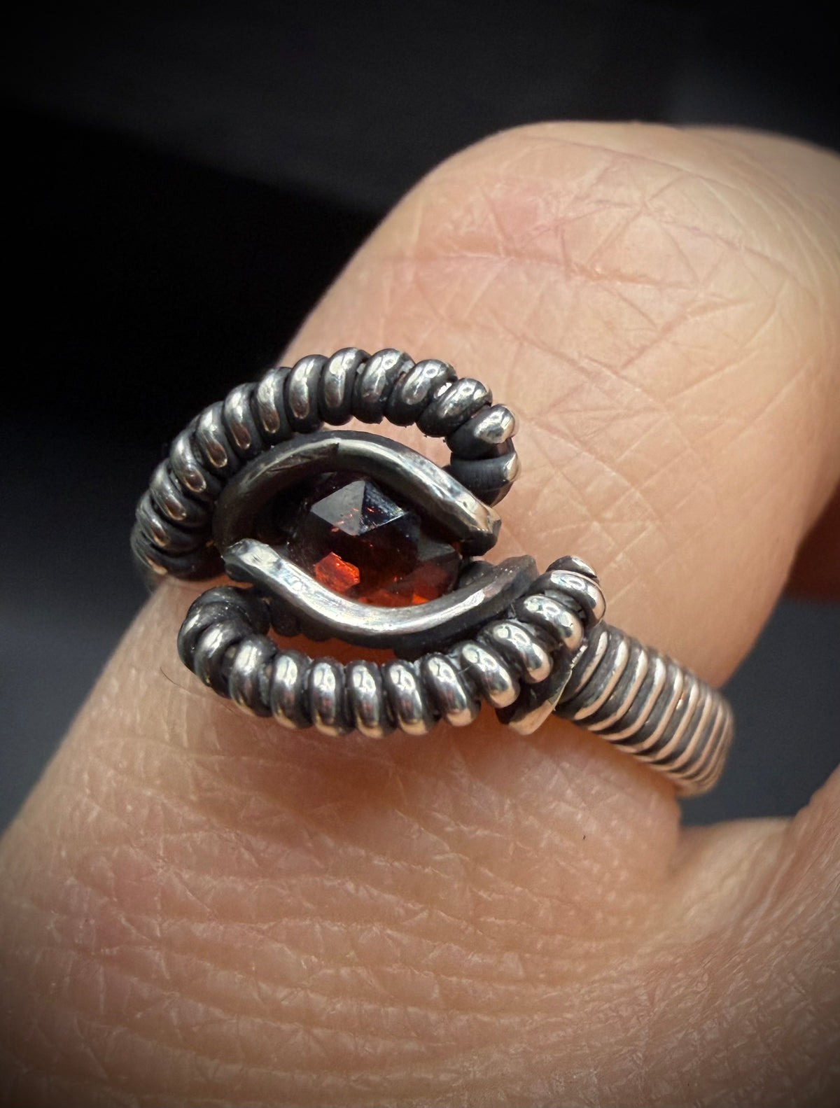 Close-up of a wire-wrapped sterling silver ring with a faceted red garnet gemstone, worn on a finger.