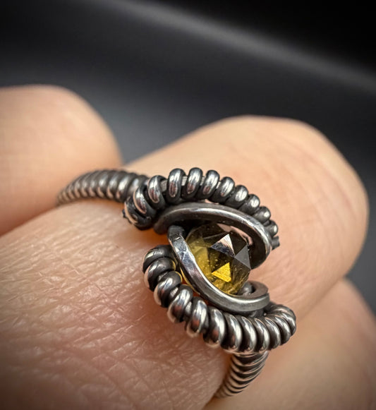 A close-up of a hand wearing a textured silver ring with a faceted yellow gemstone.