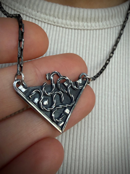 Close up view of a hand holding the silver Thoth Pendant showcasing its sharp triangular frame and intricate dark oxidized interior wirework.