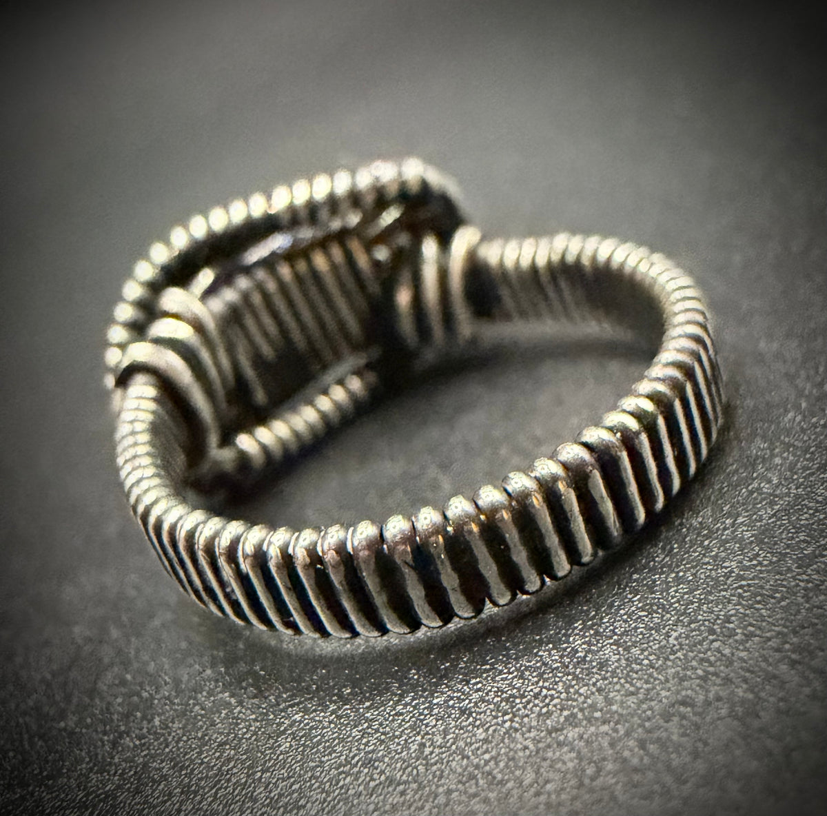 Extreme close up showing the detailed sterling silver wire wrapped band of the Asteria Ring on a dark textured surface.