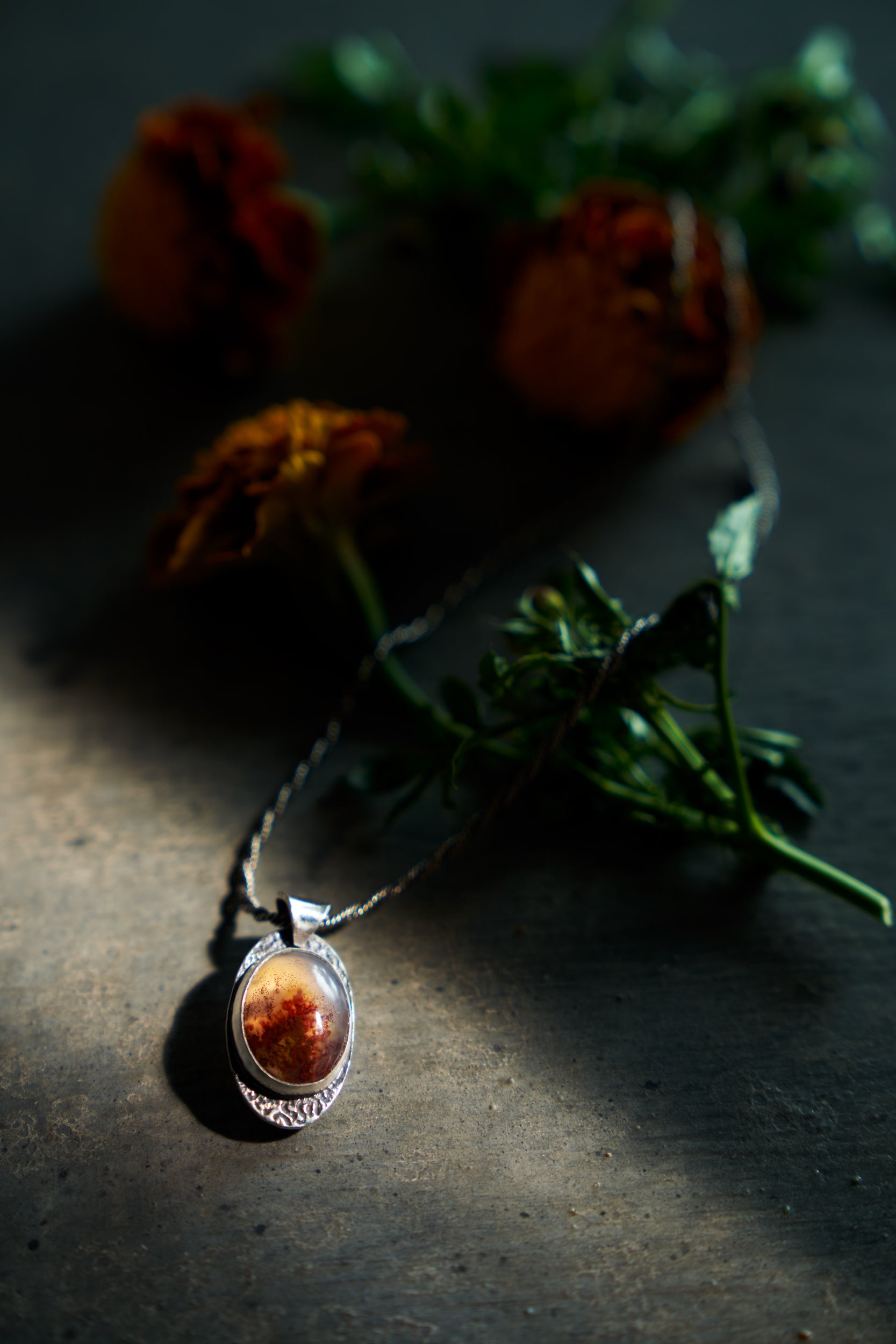 Silver pendant with an orange stone on a dark surface with flowers