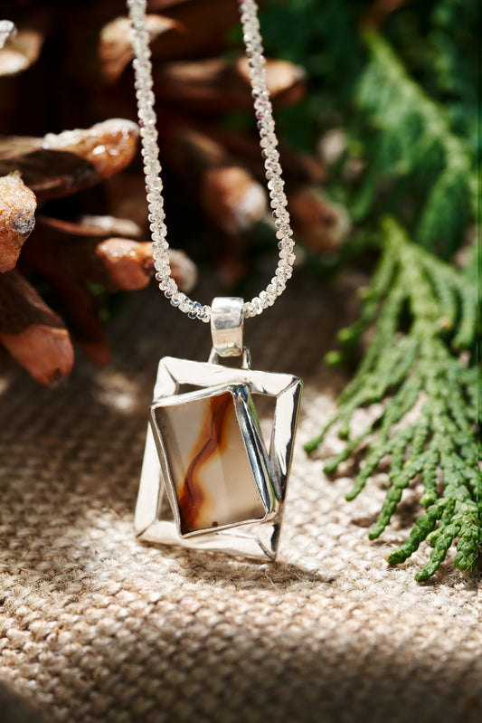 Necklace with a geometric pendant on a textured surface with greenery