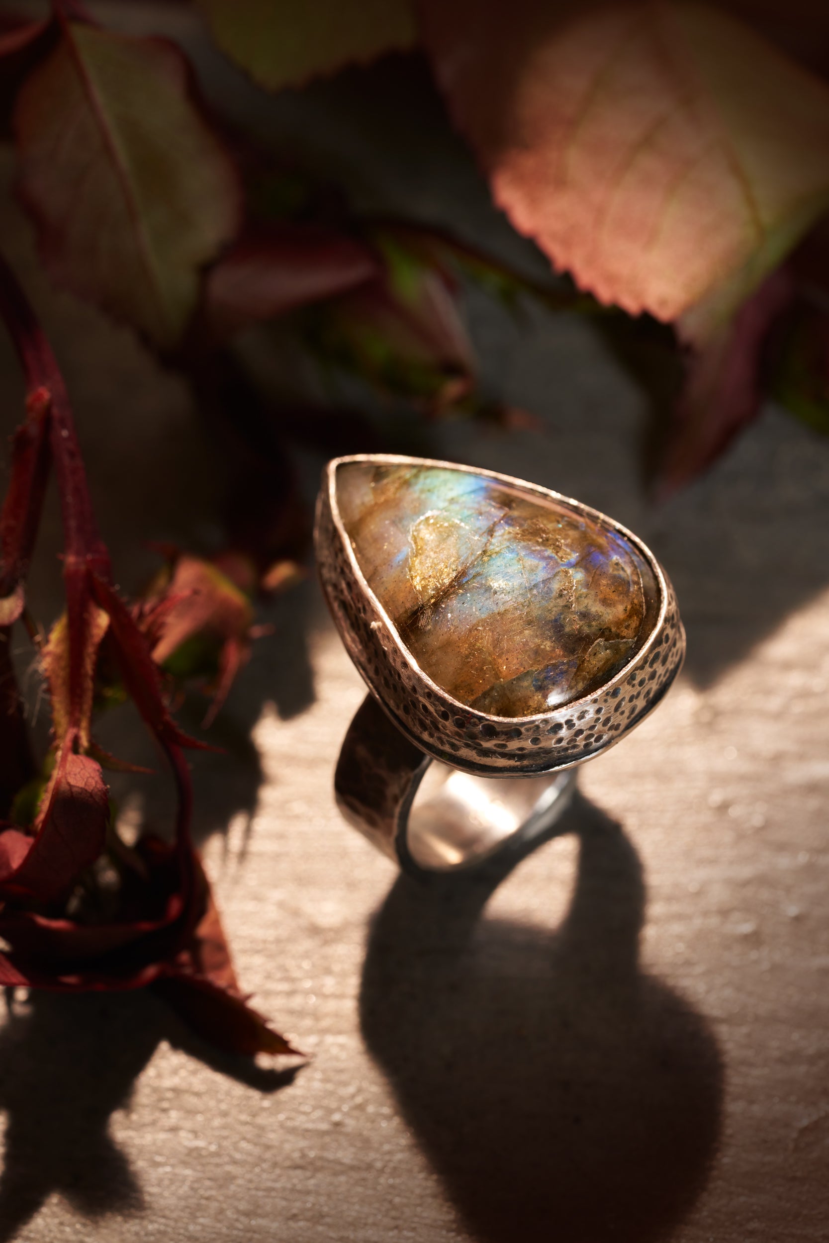 Silver ring with a large, teardrop-shaped labradorite stone on a textured surface with leaves in the background.