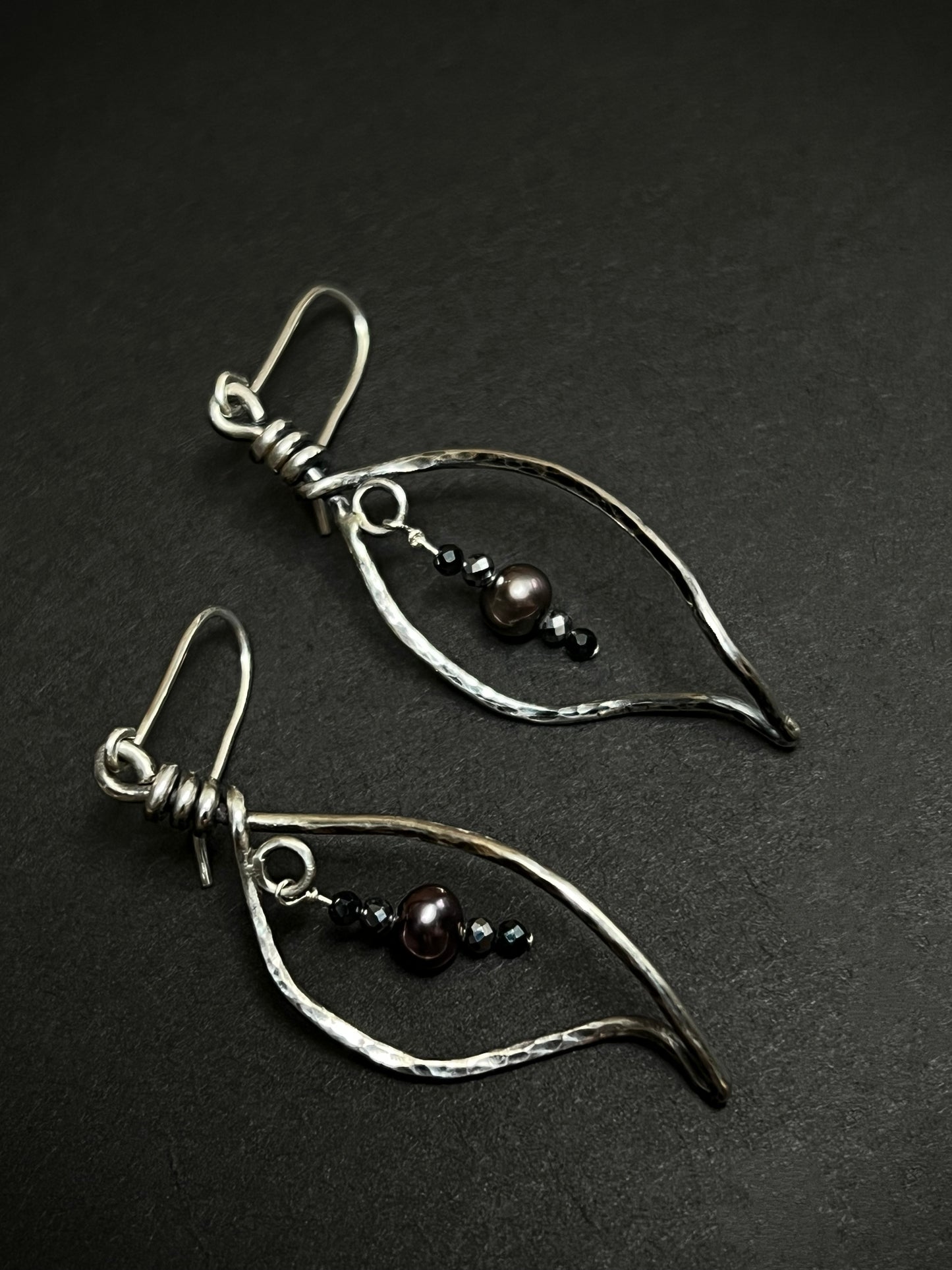 Pair of silver leaf shape earrings with beads on a dark background
