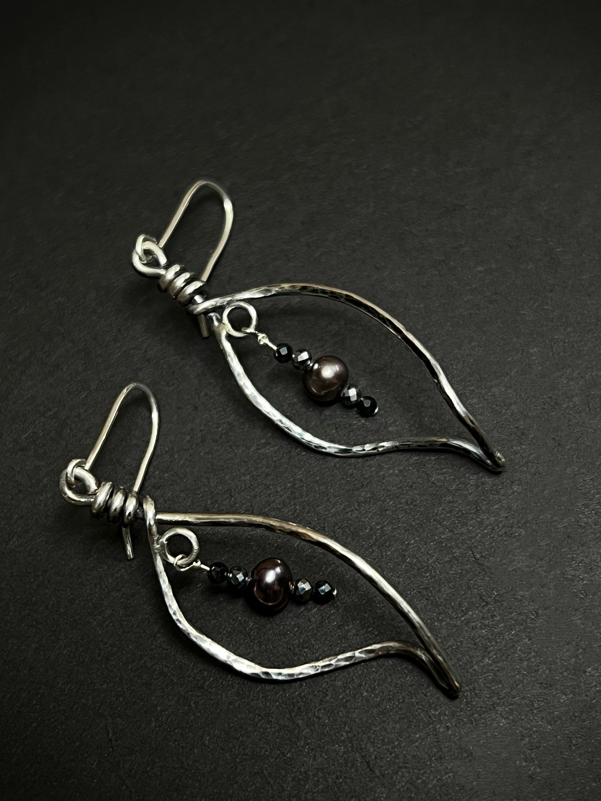 Pair of silver leaf shape earrings with beads on a dark background