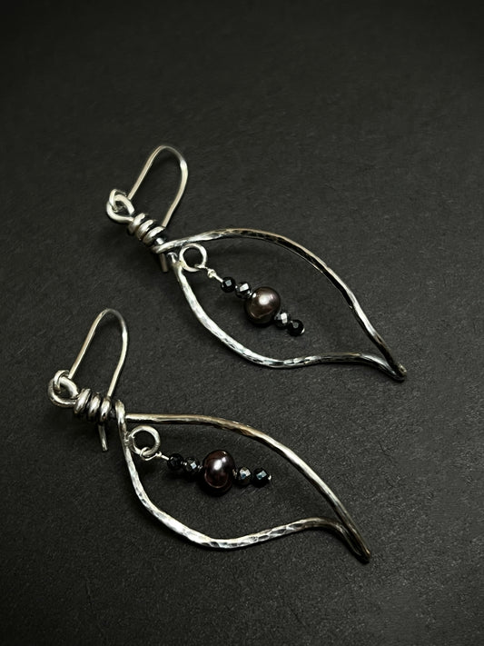 Pair of silver leaf shape earrings with beads on a dark background
