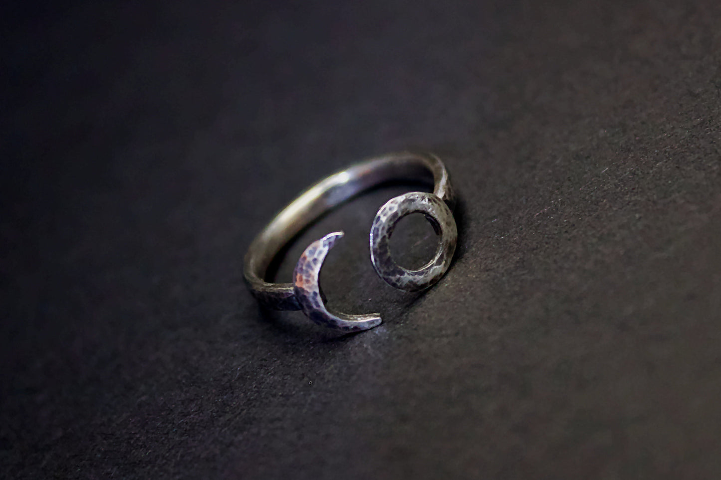 Silver ring with moon and circle design on a dark surface