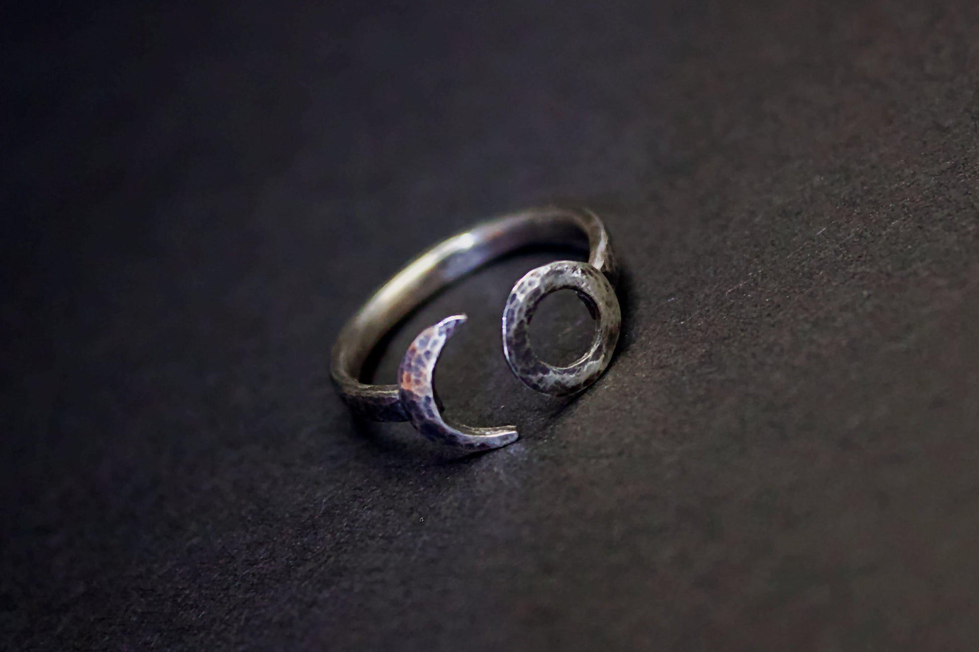 Silver ring with moon and circle design on a dark surface