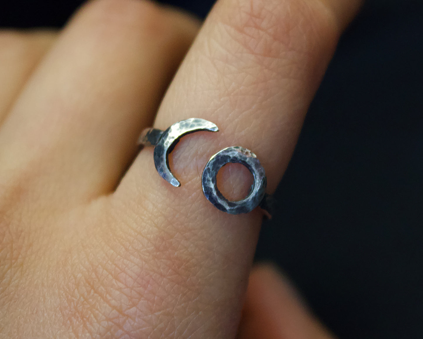 Close-up of a hand wearing two silver rings with a dark background