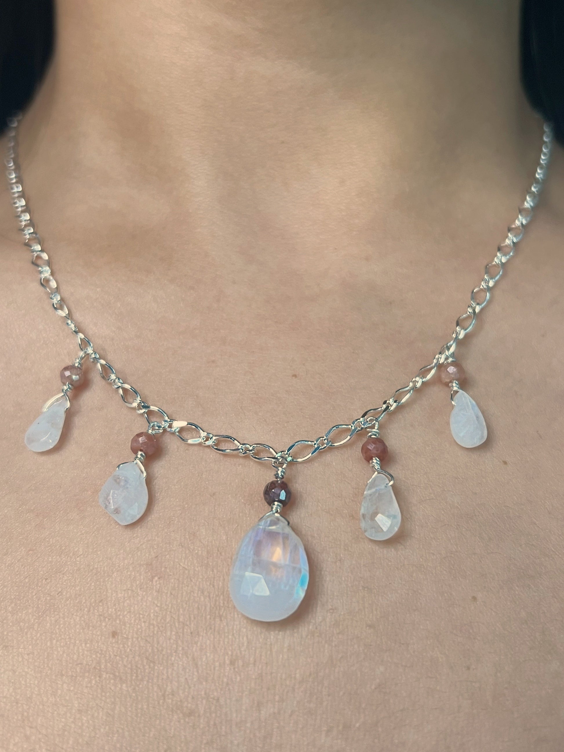 A person wearing the handcrafted Elara Necklace featuring large teardrop rainbow moonstone pendants and small round peach moonstone beads on a sterling silver chain.