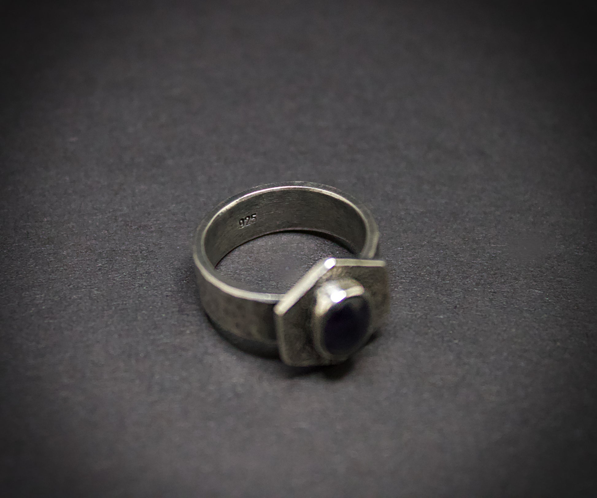 Silver ring with a dark gemstone on a gray background