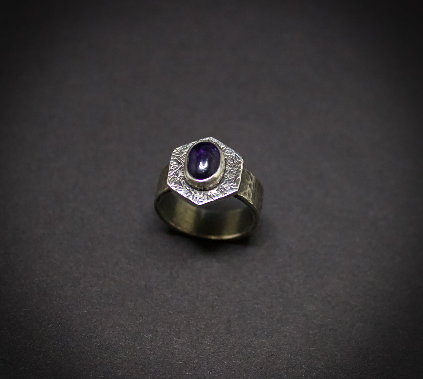 Silver ring with a purple gemstone on a dark gray background