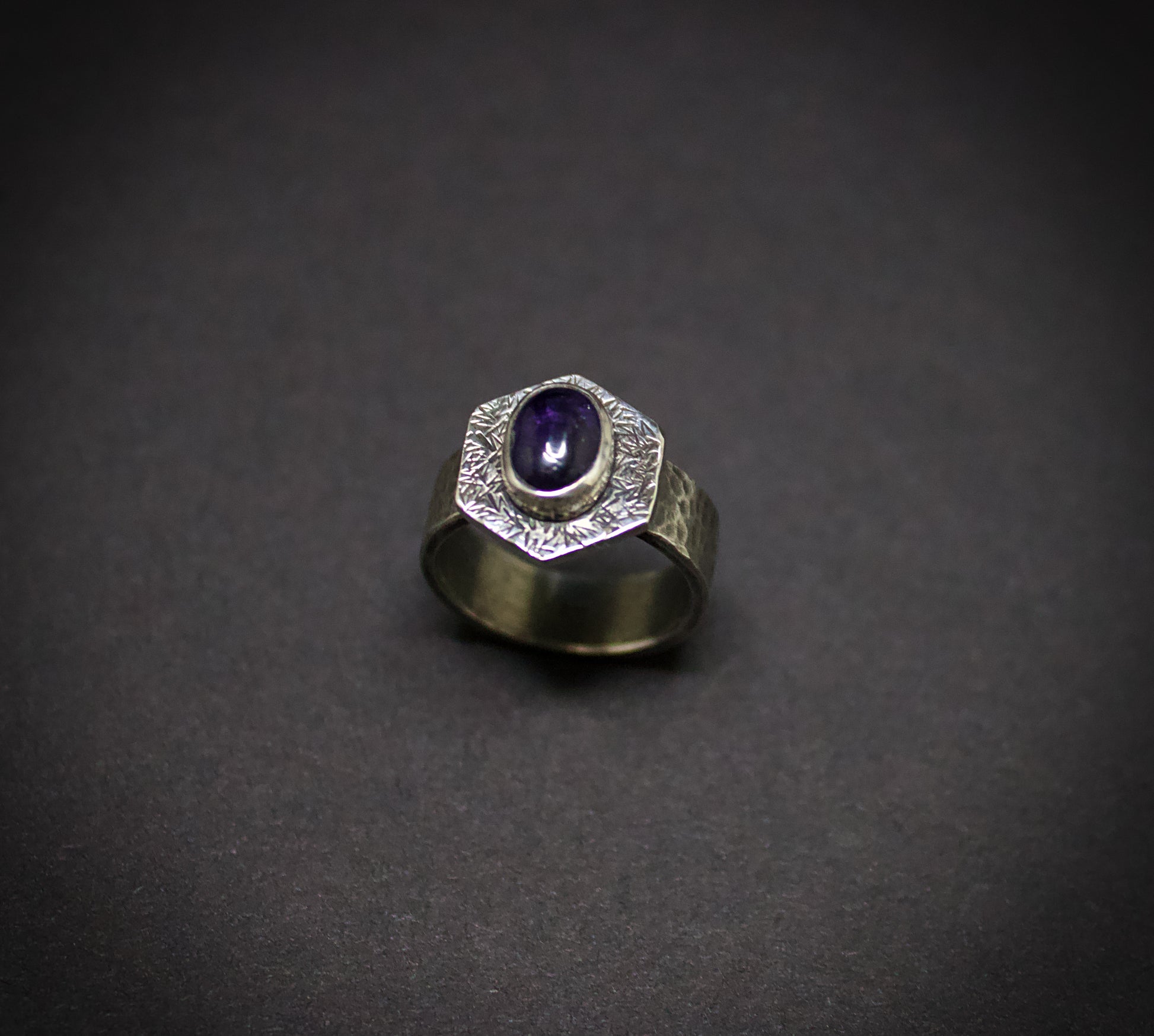 Silver ring with a purple gemstone on a dark gray background