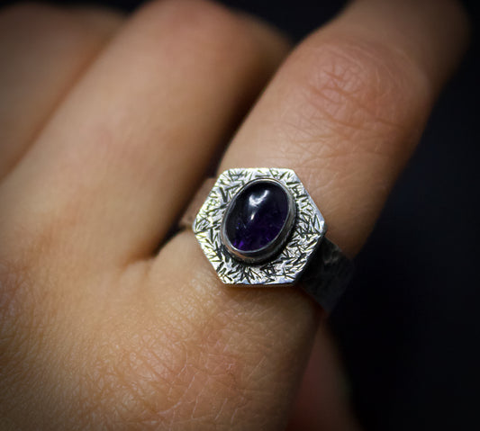 Silver ring with an iolite stone on a finger against a dark background