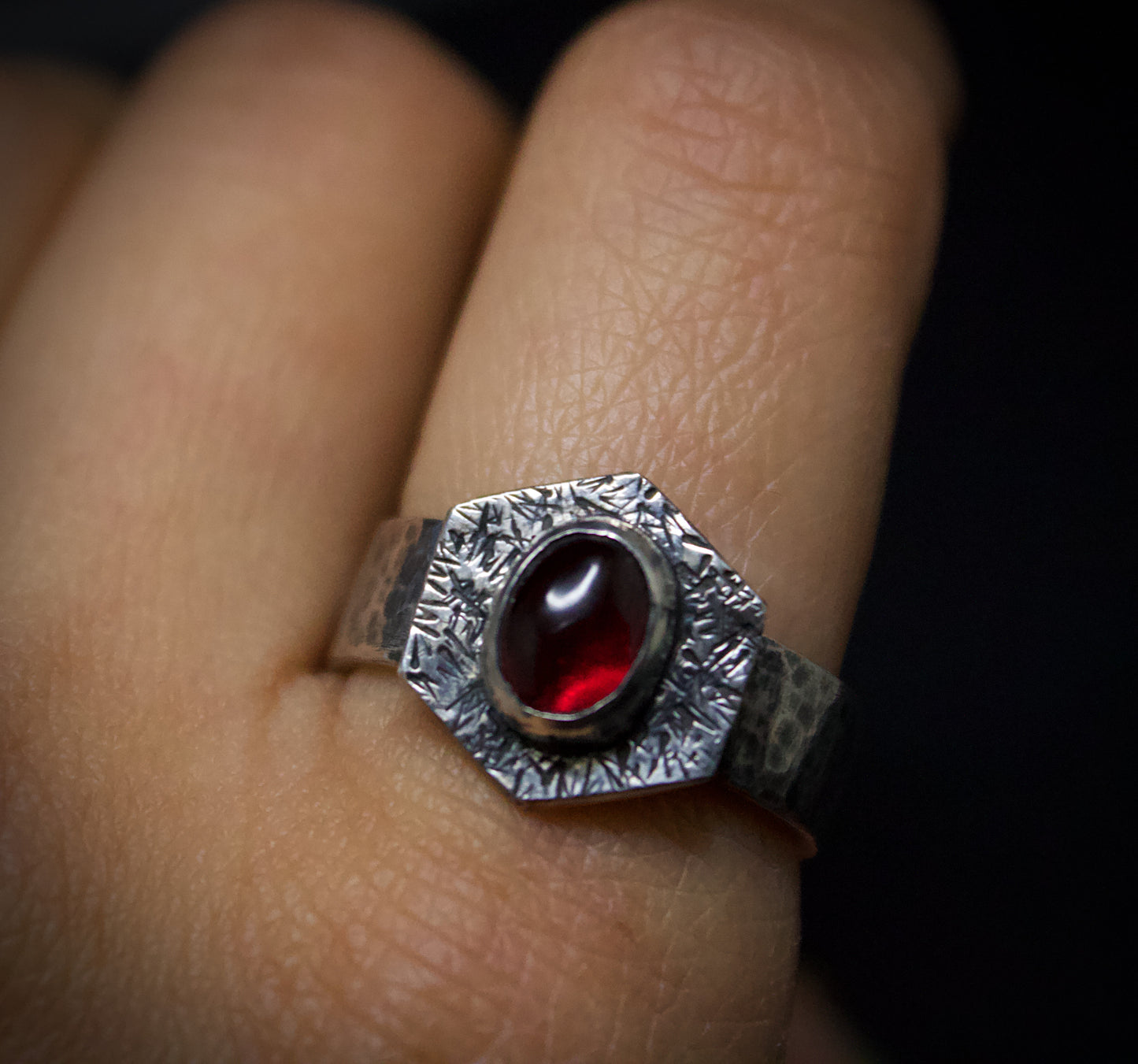Silver ring with a red gemstone on a finger against a dark background