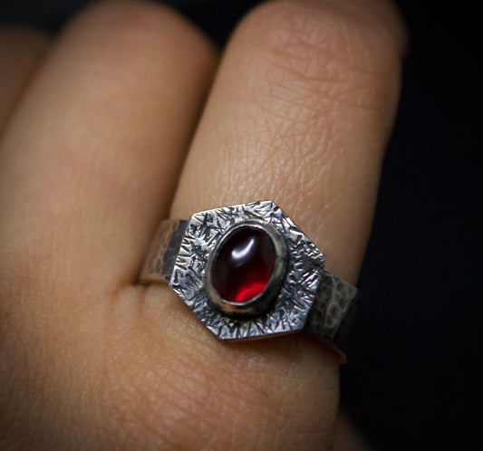 Silver ring with a red gemstone on a finger against a dark background