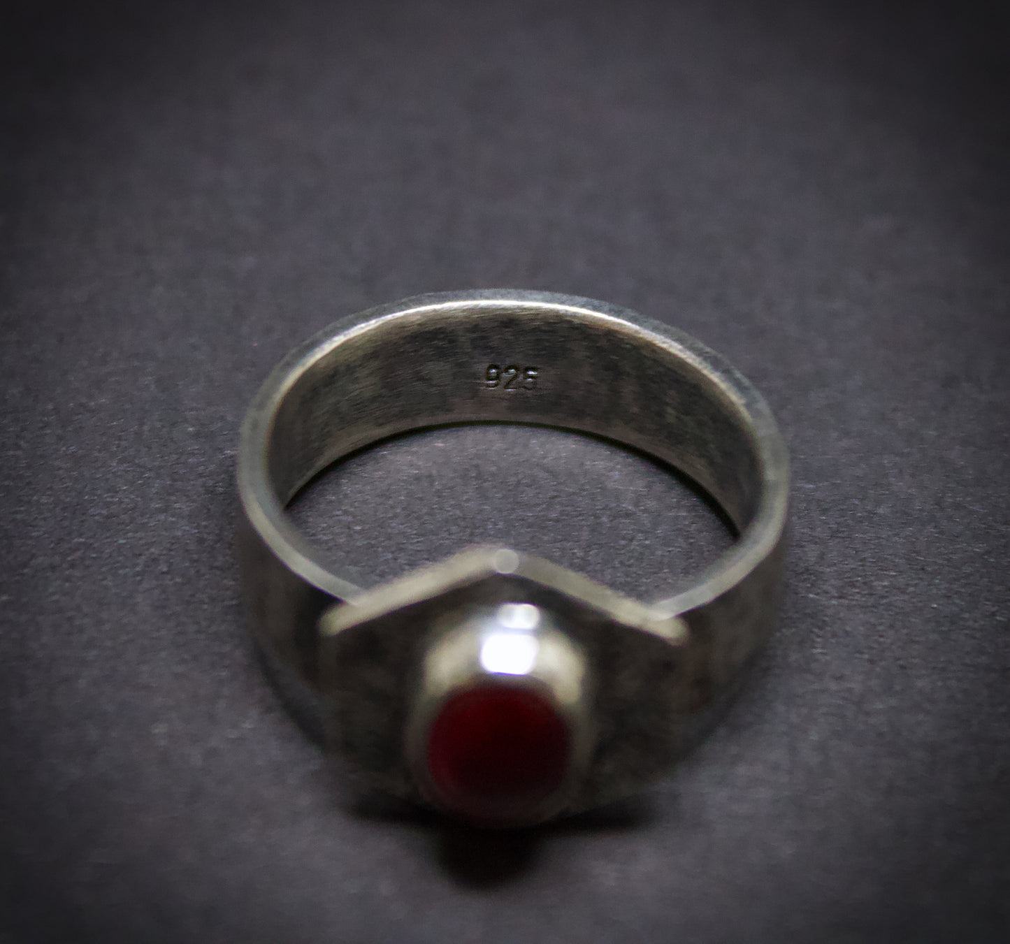 Silver ring with a red stone on a dark background. Showcasing its '925' stamp