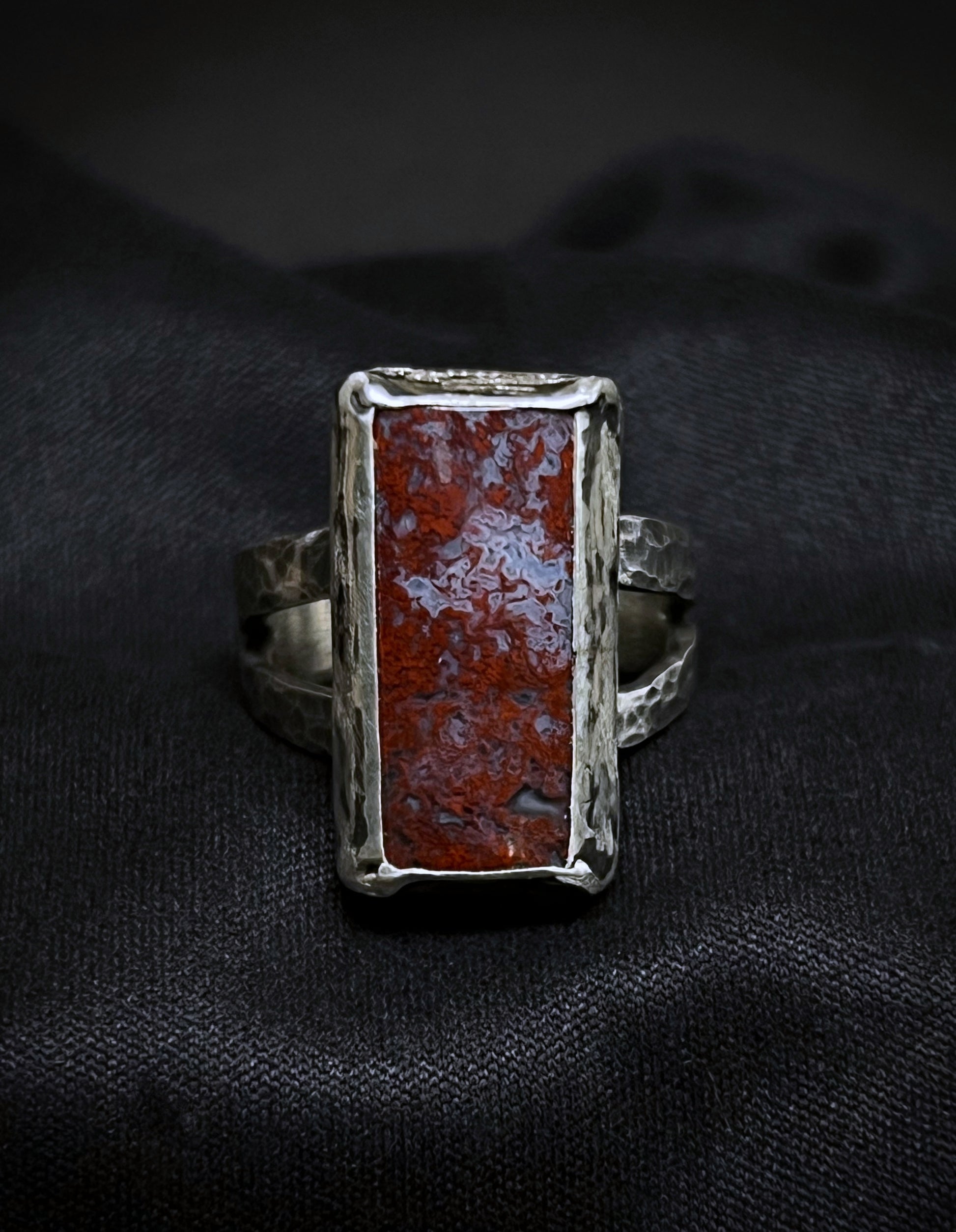 Silver ring with a red stone on a black fabric background