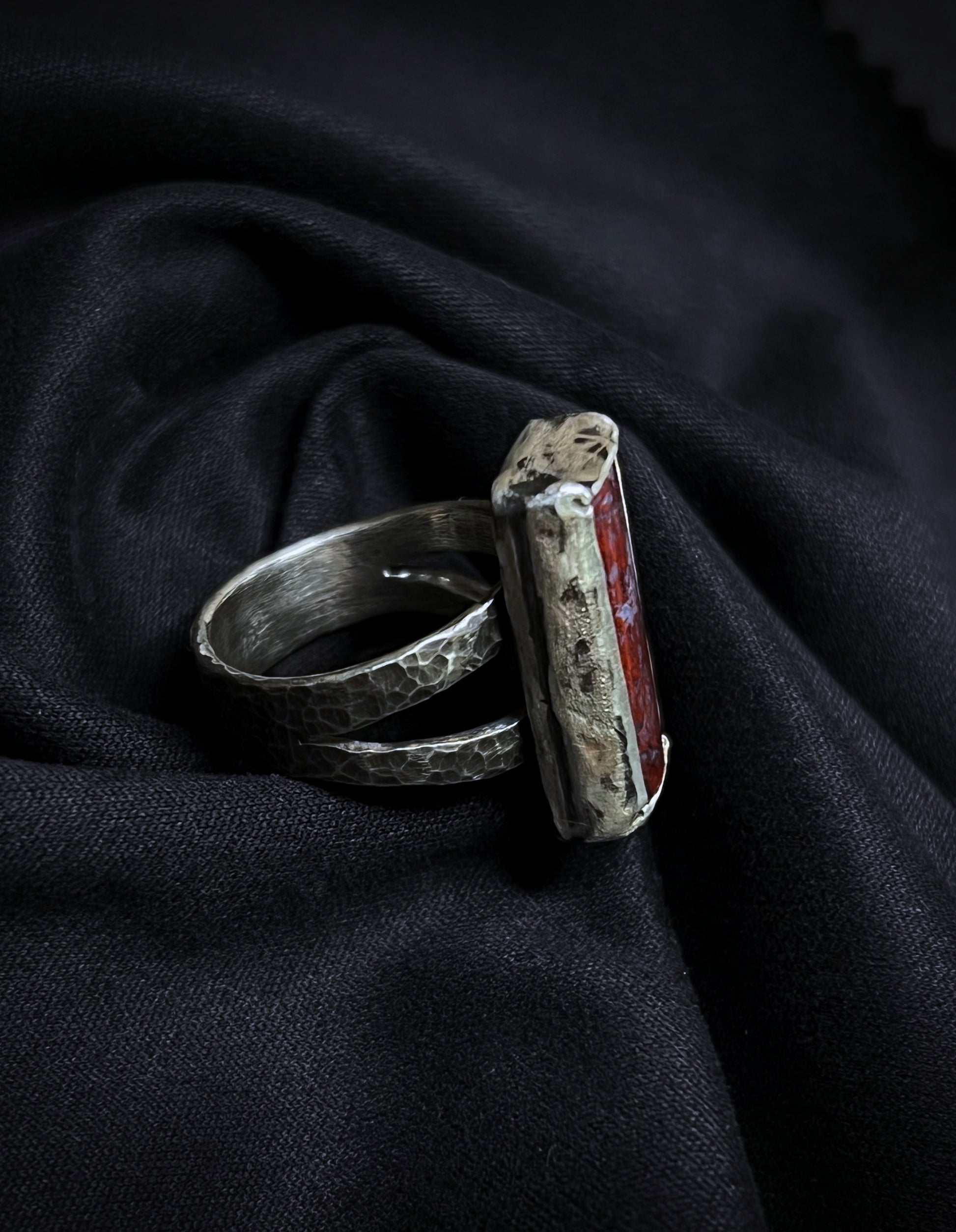 Silver ring with a red stone on a dark fabric background