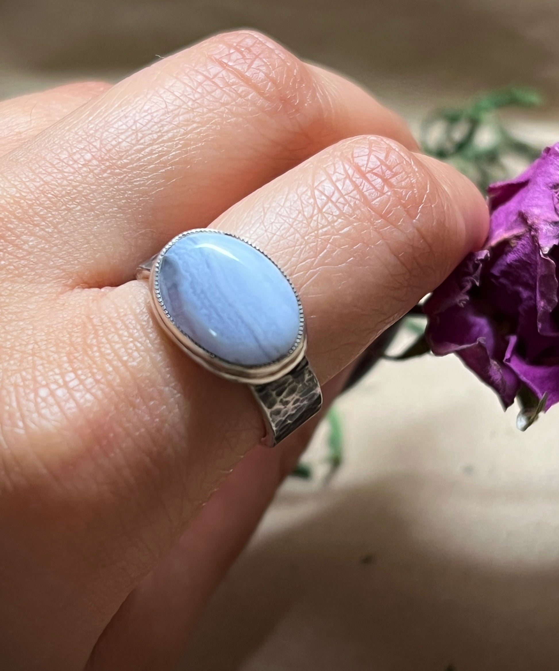 Hand wearing a ring with a blue stone against a blurred background