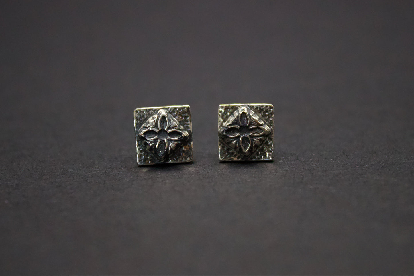 Pair of silver square earrings with floral design on a dark background