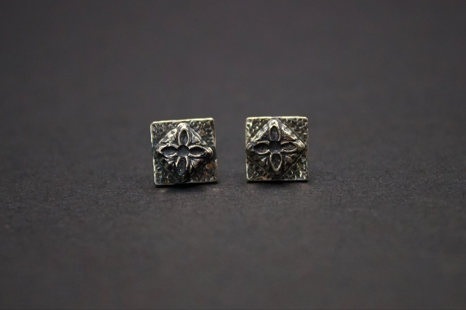 Pair of silver square earrings with floral design on a dark background