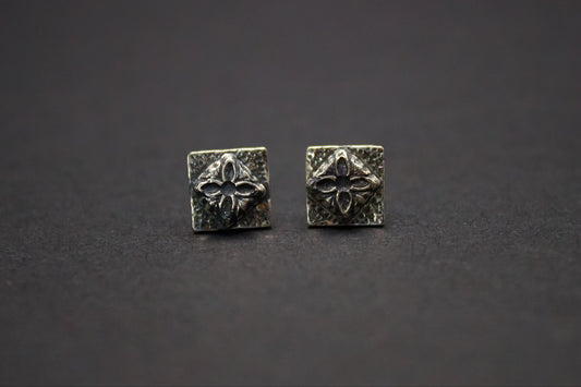 Pair of silver square earrings with floral design on a dark background