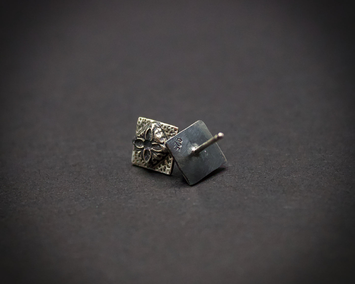 Pair of silver square earrings with floral design on a dark gray background showing its .925 stamp (no hallmark stamp)