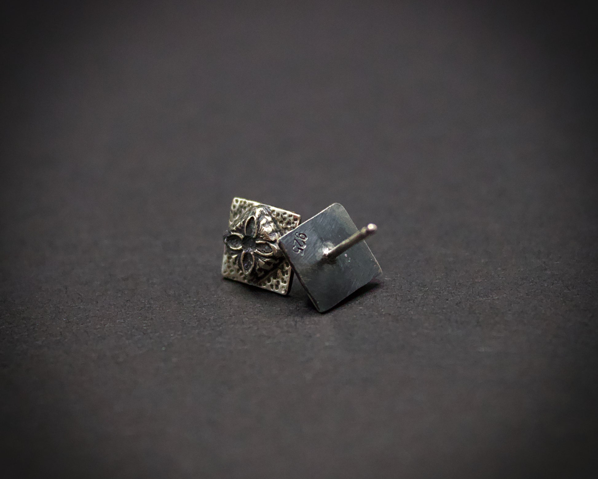 Pair of silver square earrings with floral design on a dark gray background showing its .925 stamp (no hallmark stamp)