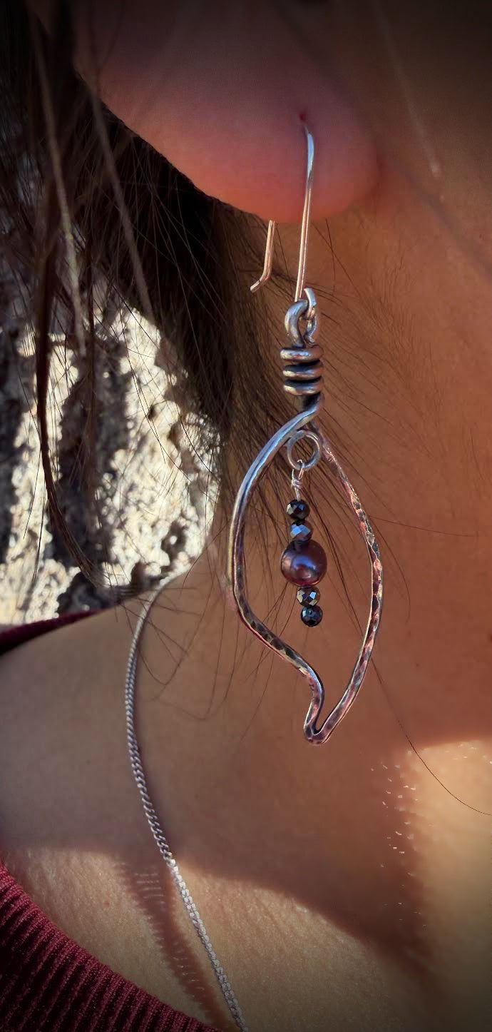 Silver earrings with beads worn by a person against a blurred natural background