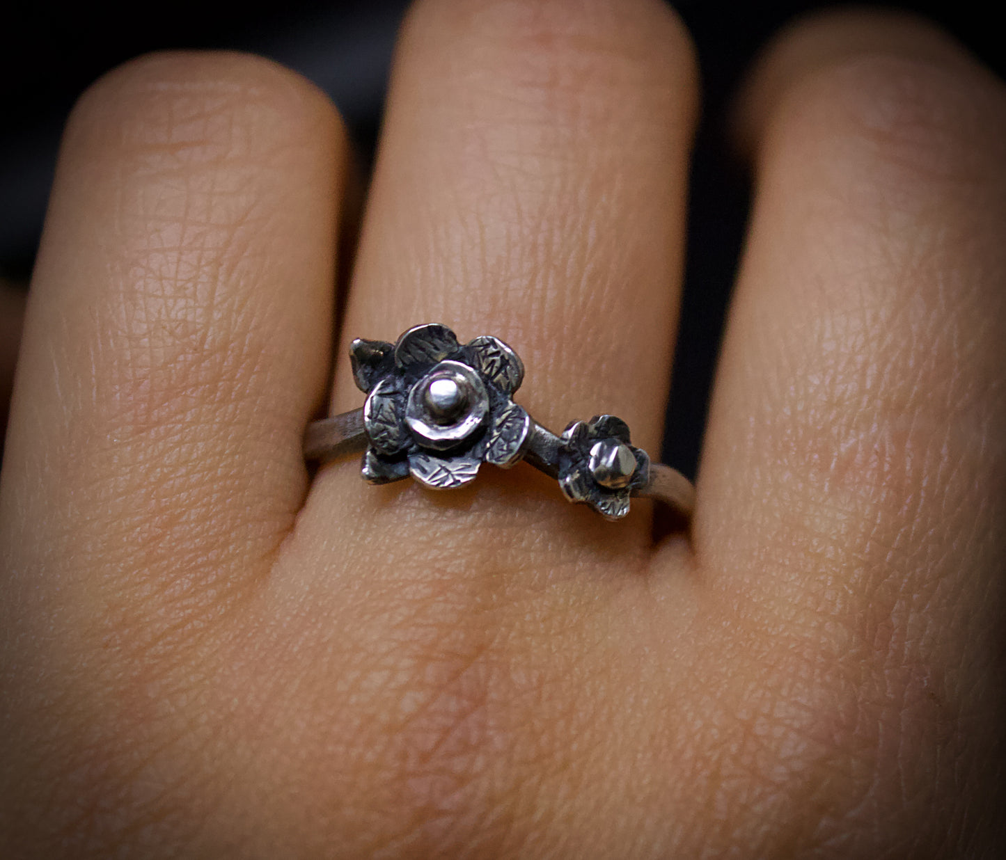 Silver floral ring on a finger with a dark background