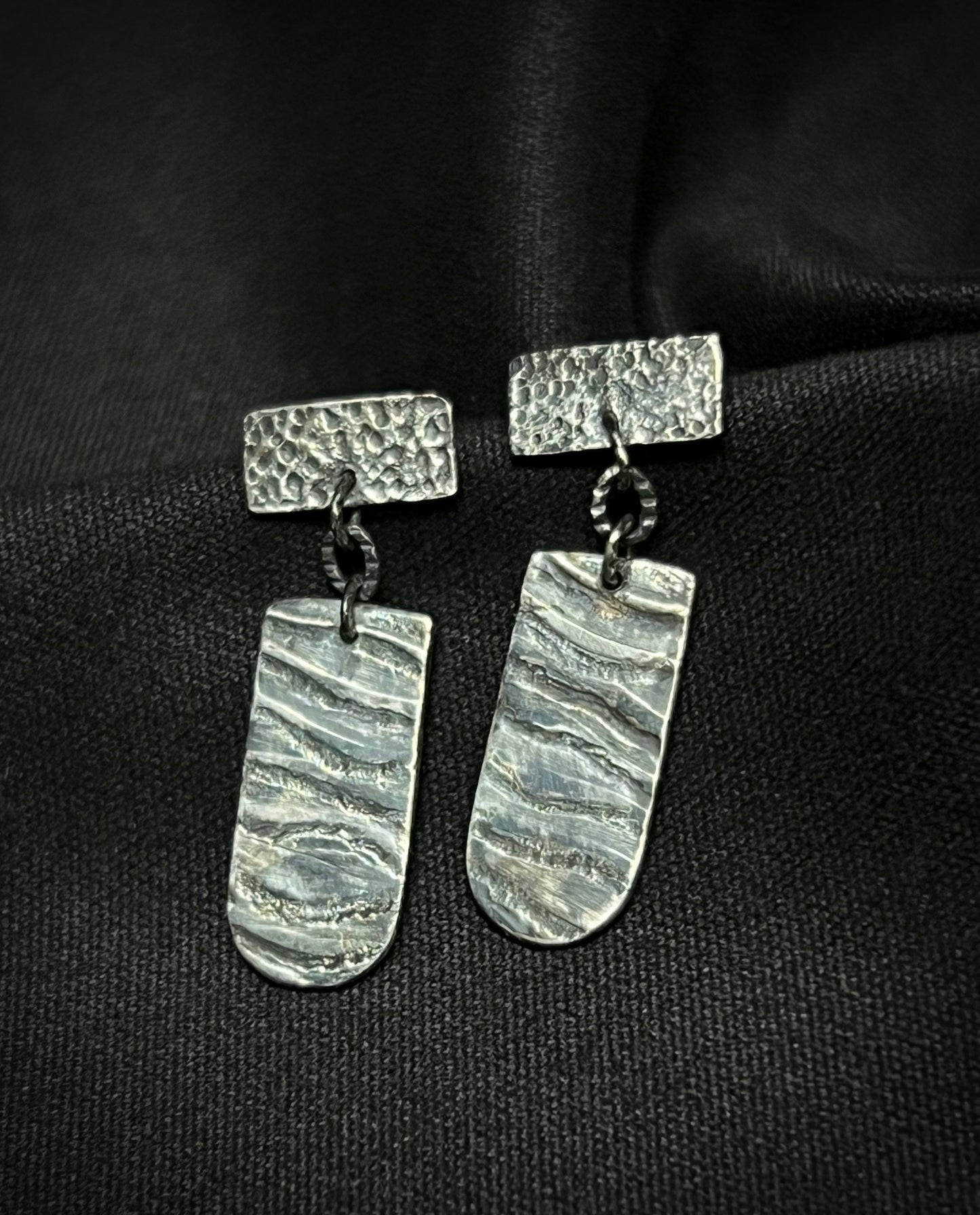 Pair of silver earrings with textured design on a black background